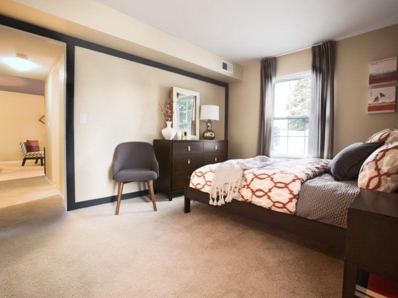 This image shows the bedroom area featuring a stylish boudoir chair beside the bedroom and a passageway directly through the living room.